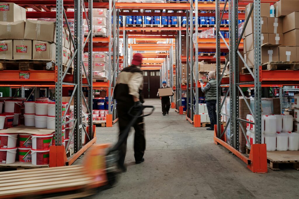 Warehouse interior with workers organizing shelves full of boxes and containers.